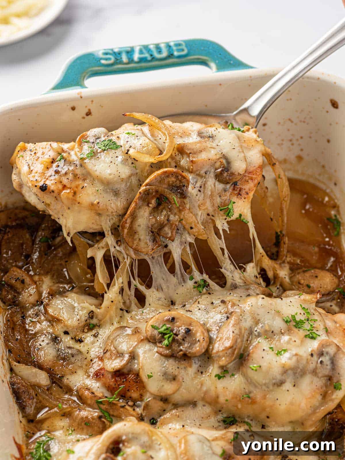 A spoon scooping up a piece of cheesy baked mushroom chicken from the baking dish, showing the gooey cheese and tender chicken.
