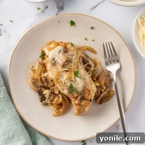 Overhead view of a plate of cheesy baked chicken breasts with mushrooms with a fork on the plate.