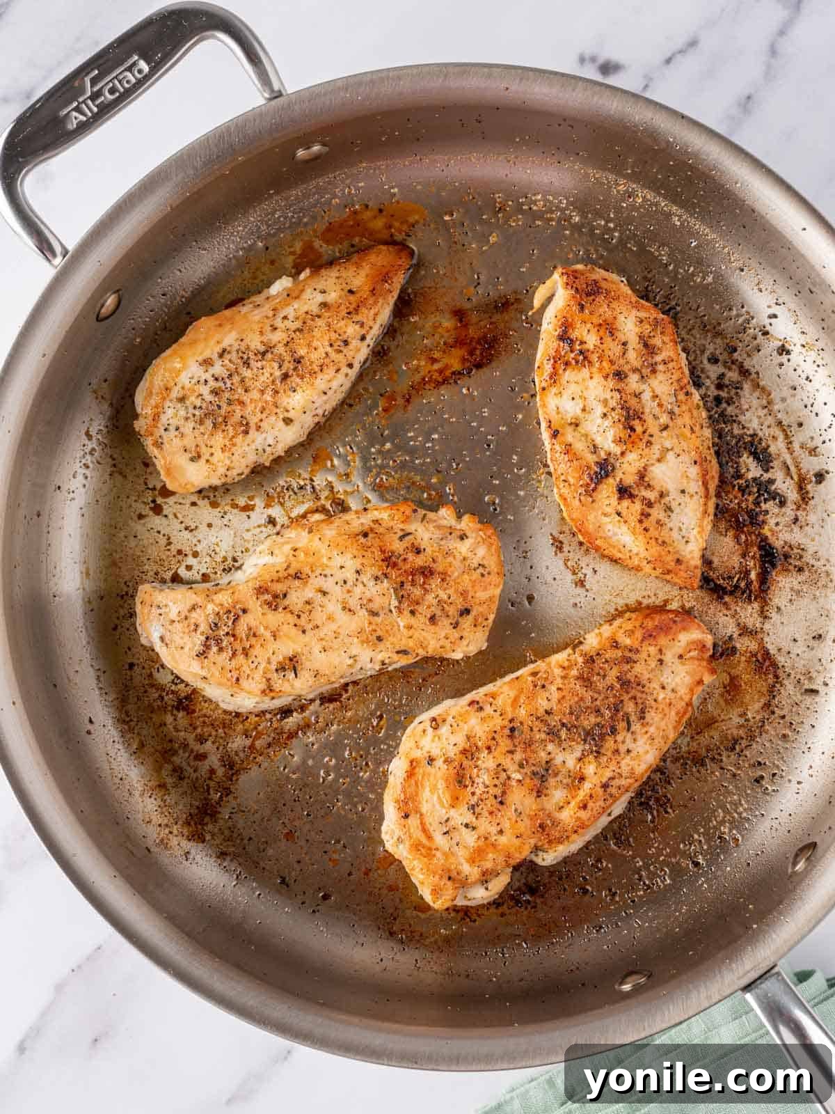 Overhead view of seasoned chicken breasts searing in a large skillet until golden brown.