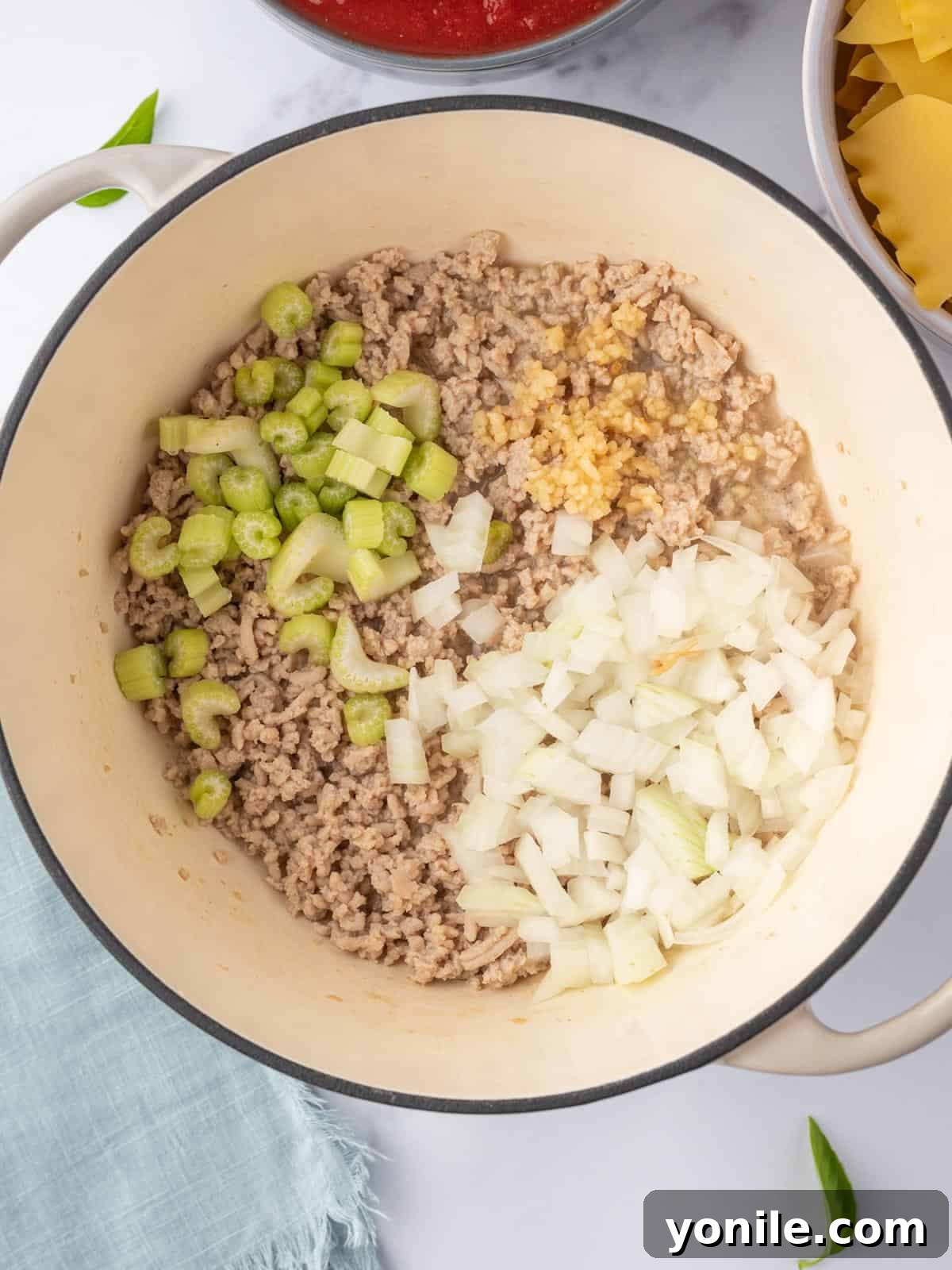 Process photo showing onion, celery, and garlic being added to browned chicken in a pot.