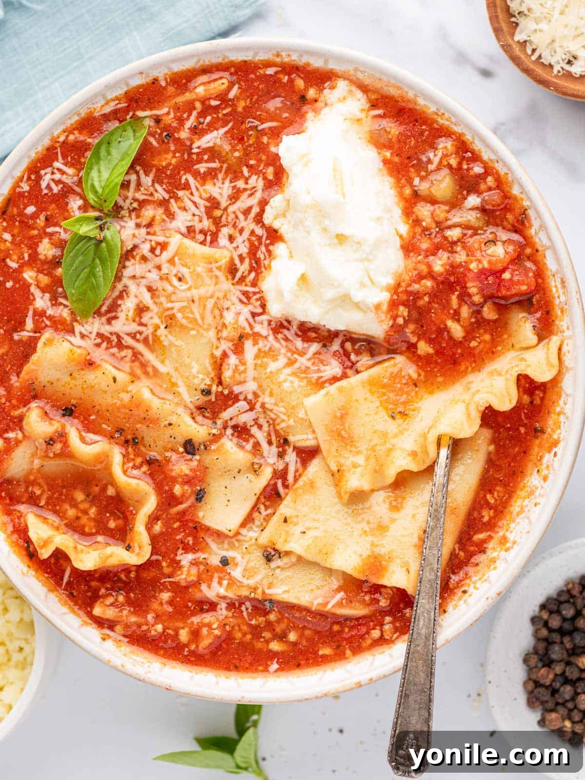 A silver spoon in a bowl of easy lasagna soup with basil leaves, parmesan cheese and a dollop of ricotta cheese, ready to be eaten.