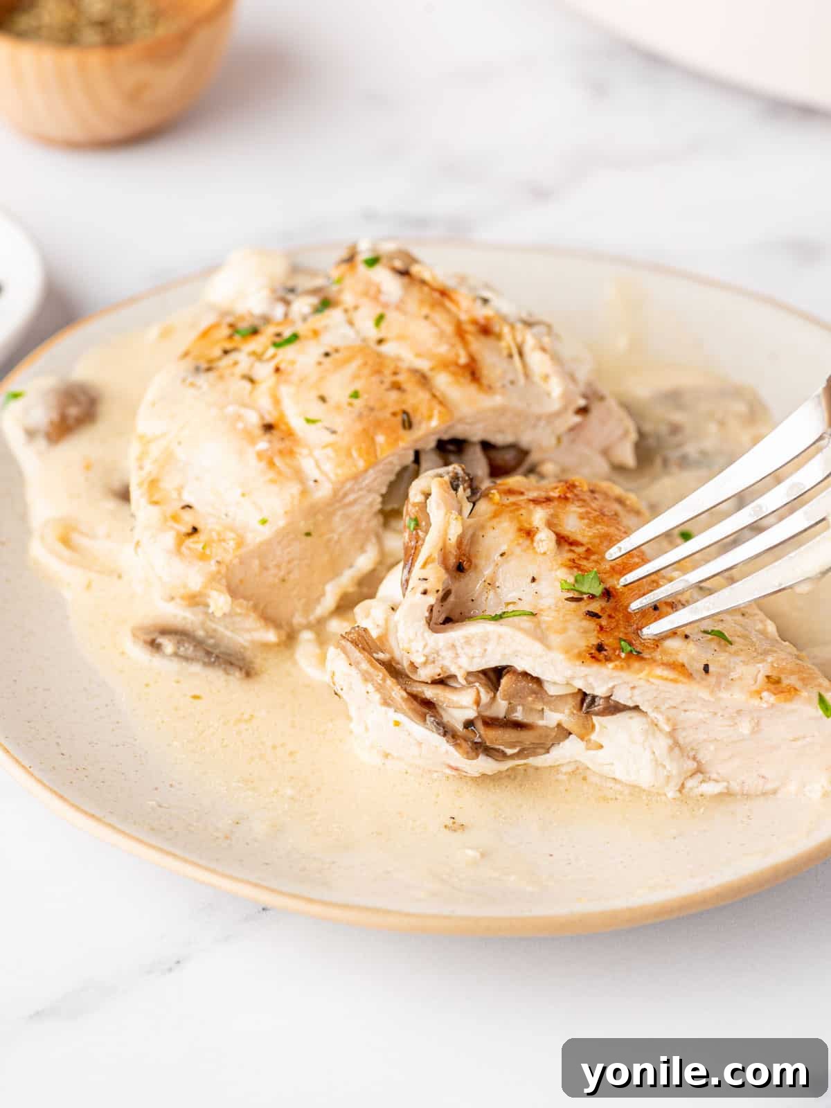 A fork is poised over a bite sized piece of chicken on a plate of mushroom stuffed chicken.