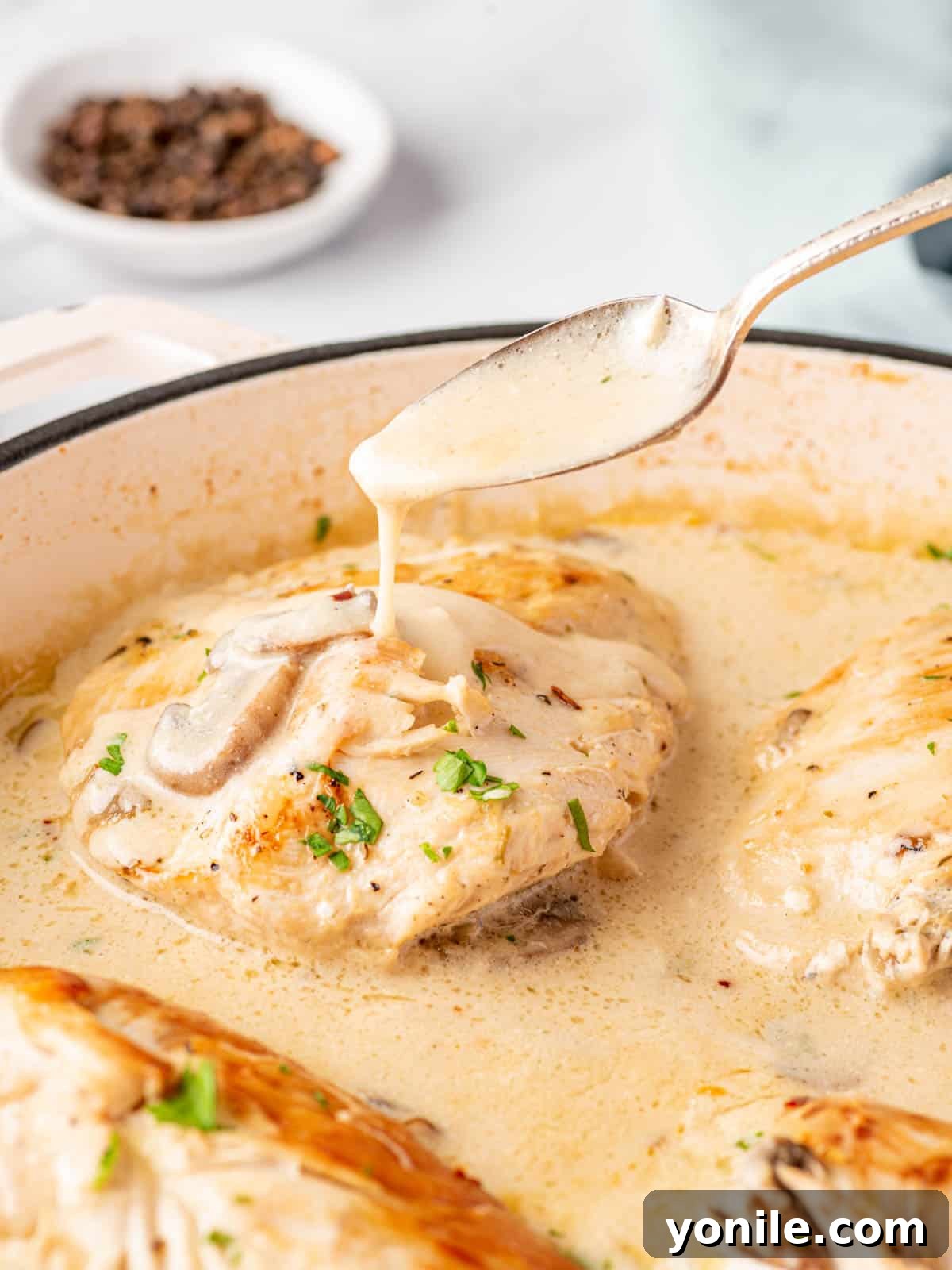 Creamy sauce is dripping off a spoon and onto stuffed chicken breast in a skillet.