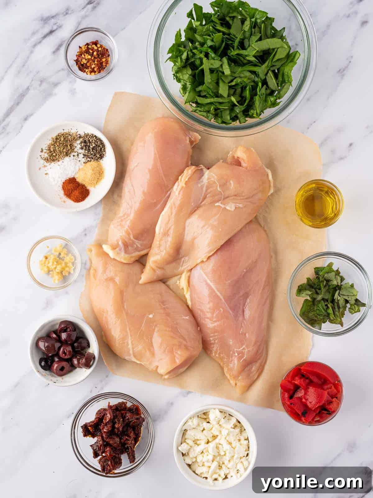 A selection of fresh and jarred ingredients laid out, including chicken breasts, spinach, feta cheese, olives, and spices, ready for making Mediterranean stuffed chicken breasts.
