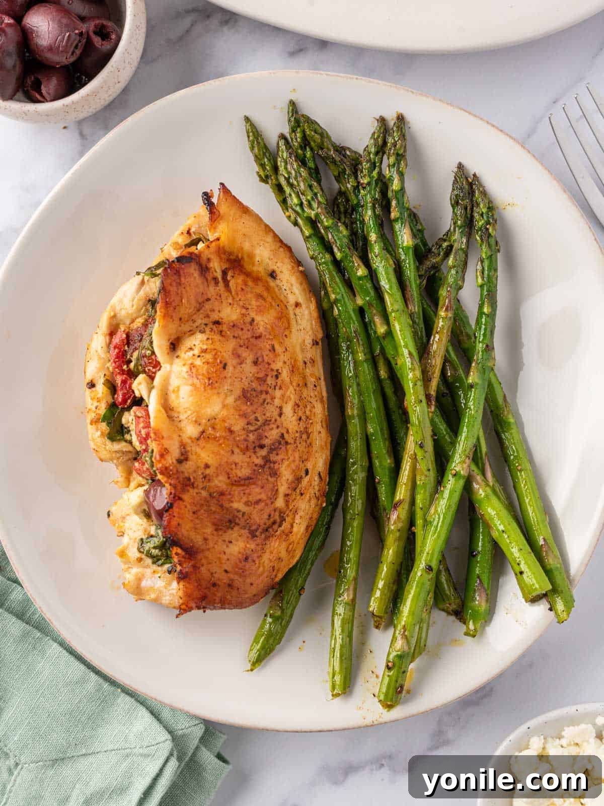 A plate featuring a sliced Mediterranean stuffed chicken breast alongside fresh asparagus, highlighting a healthy and balanced meal.