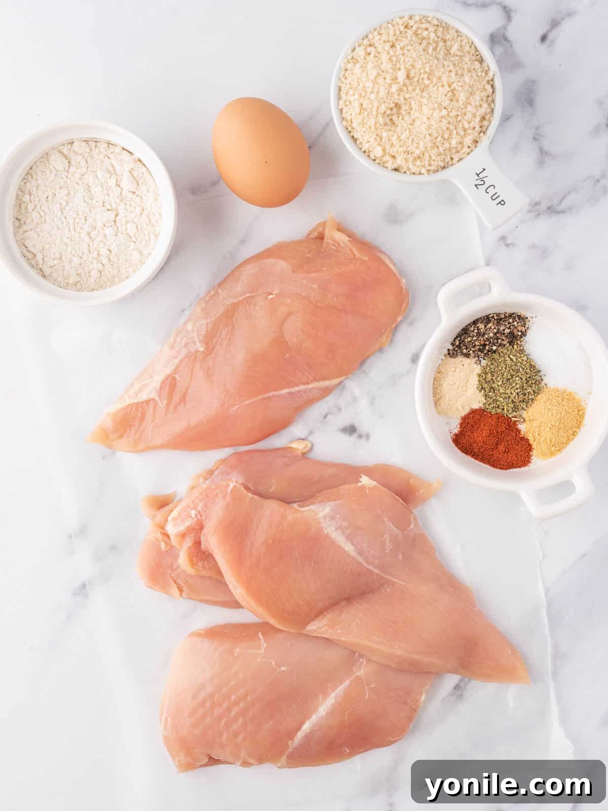 Crispy Air Fryer Chicken Cutlets 3 Ingredients for air fryer chicken cutlets laid out, including chicken breasts, flour, panko, egg, and various spices.
