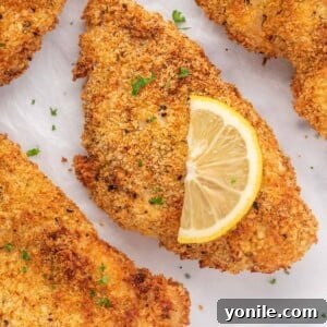 Closeup of a crispy chicken cutlet with a lemon slice on top.