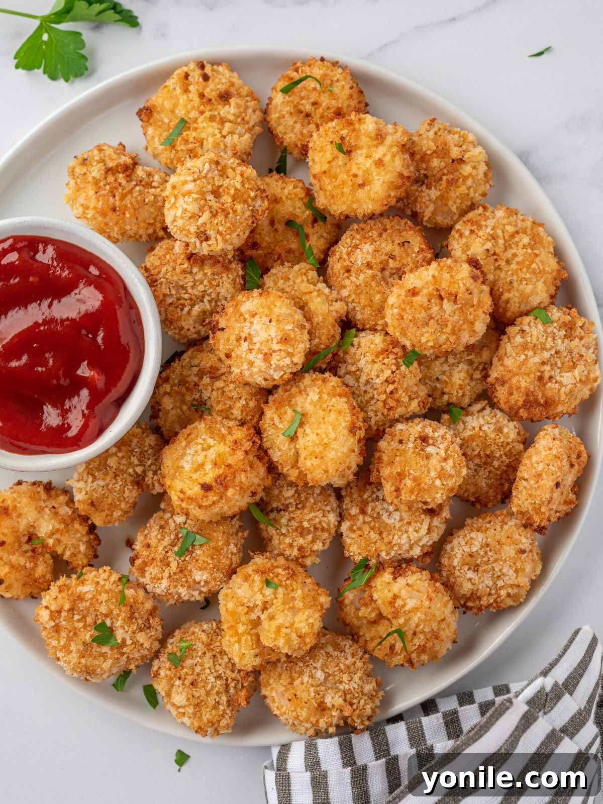A white tray of air fryer popcorn shrimp with a small bowl of cocktail sauce. 