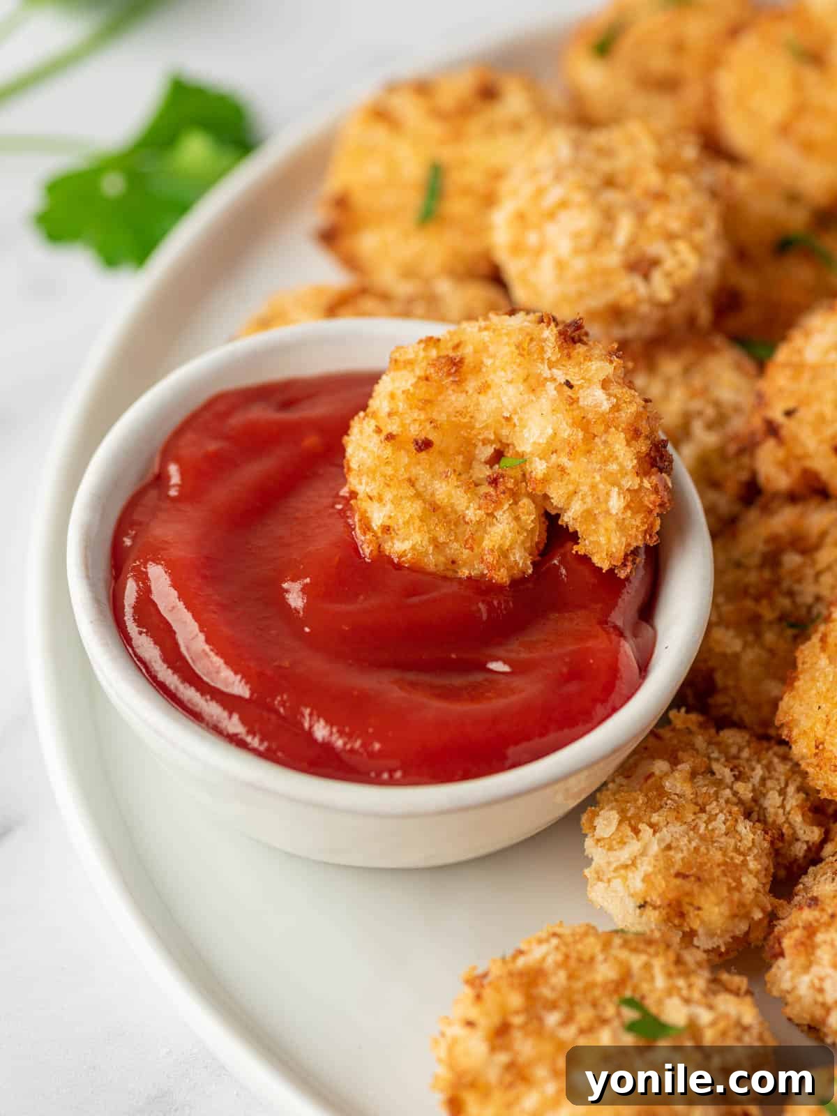 A piece of air fryer popcorn shrimp is laying in a bowl of cocktail sauce.