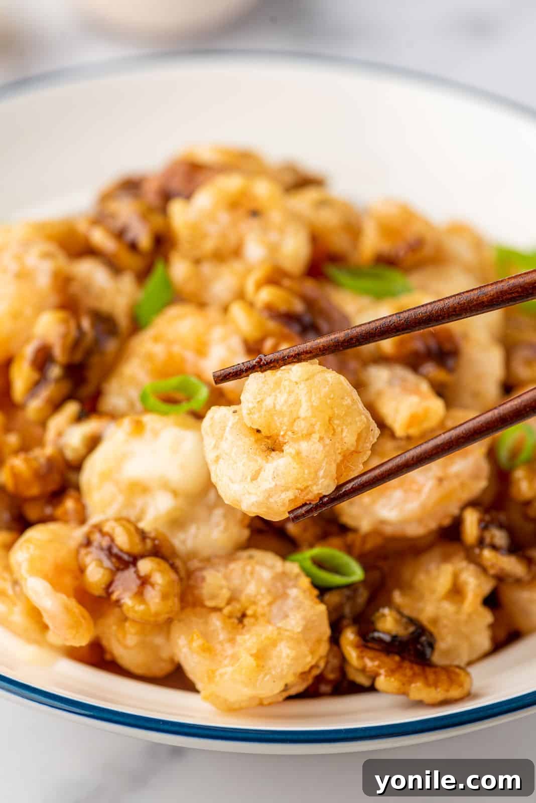 Golden Honey Walnut Shrimp 11 Chopsticks pick up a piece of copycat panda express walnut shrimp from a bowl.