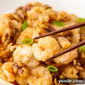 Chopsticks pick up a piece of copycat panda express walnut shrimp from a bowl.
