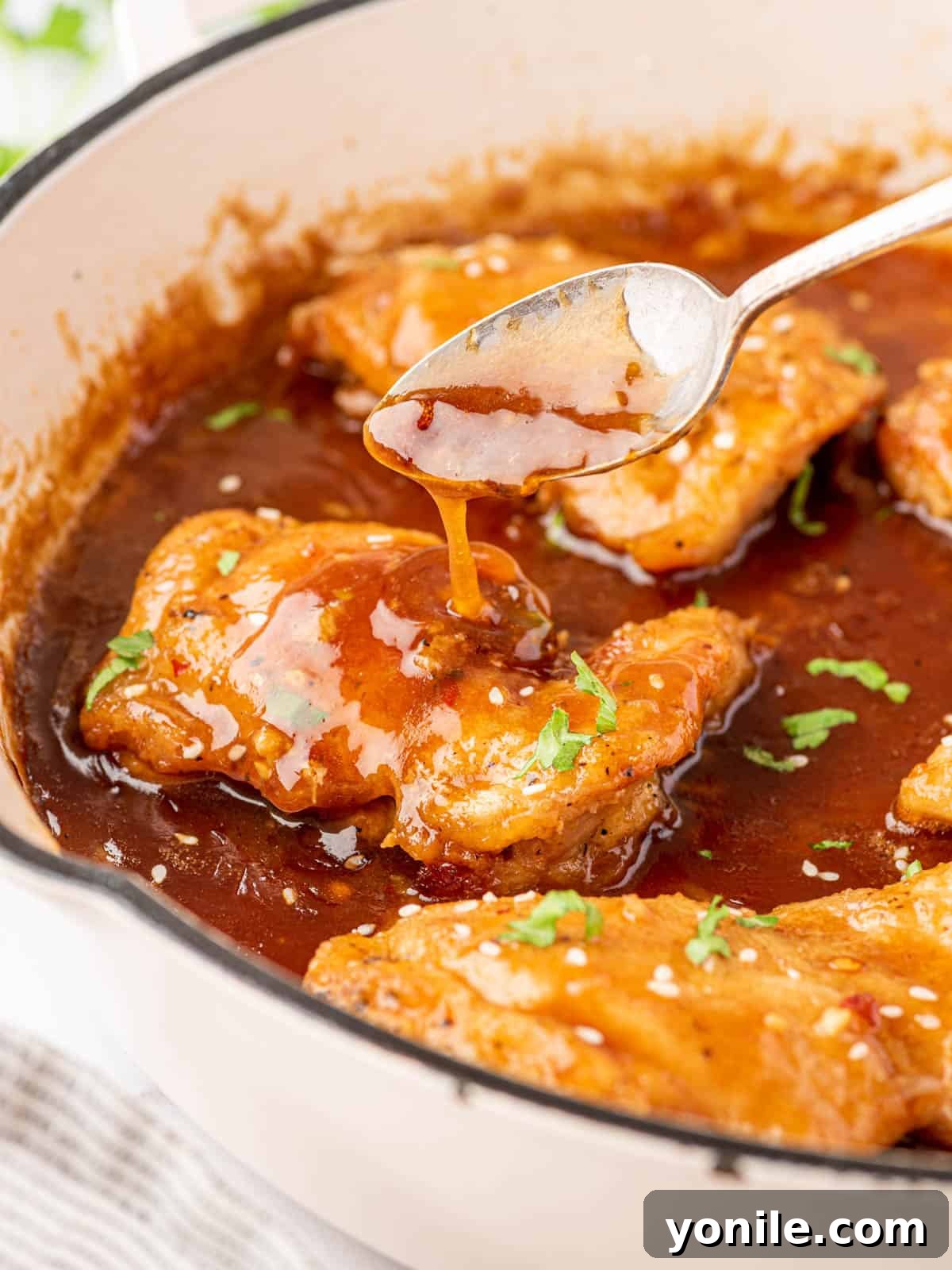 A spoonful of glossy honey garlic sauce being drizzled over a seared chicken thigh on a plate.