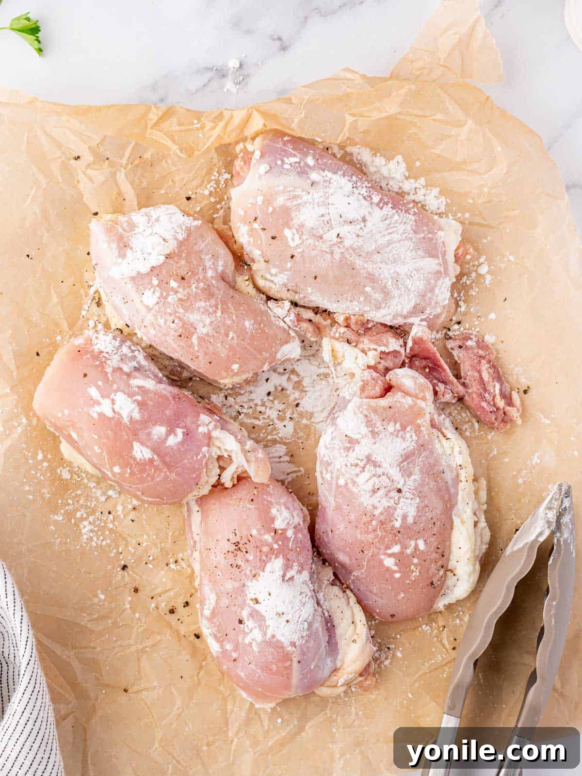 Raw chicken thighs coated evenly with a mixture of cornstarch, salt, and pepper on a cutting board.