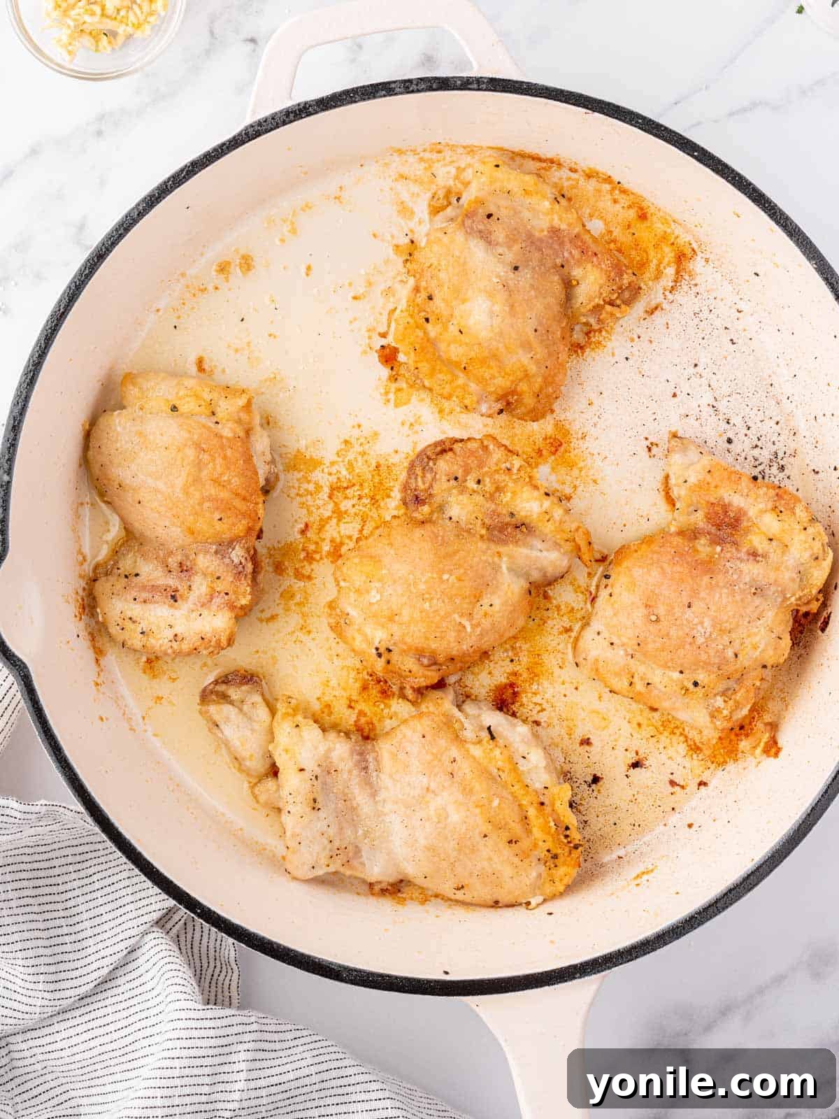 Chicken thighs searing in a hot skillet, developing a golden-brown crust.