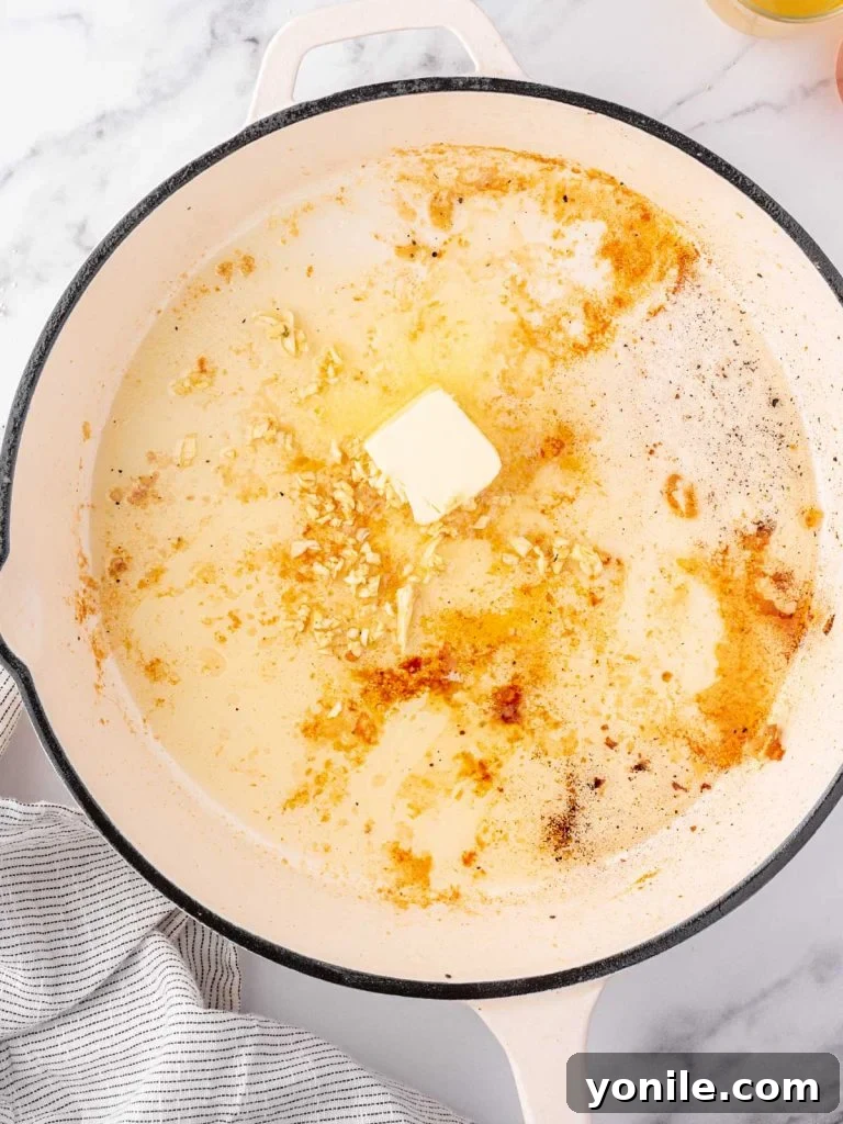 Melted butter and minced garlic sizzling in the same skillet after the chicken has been removed.