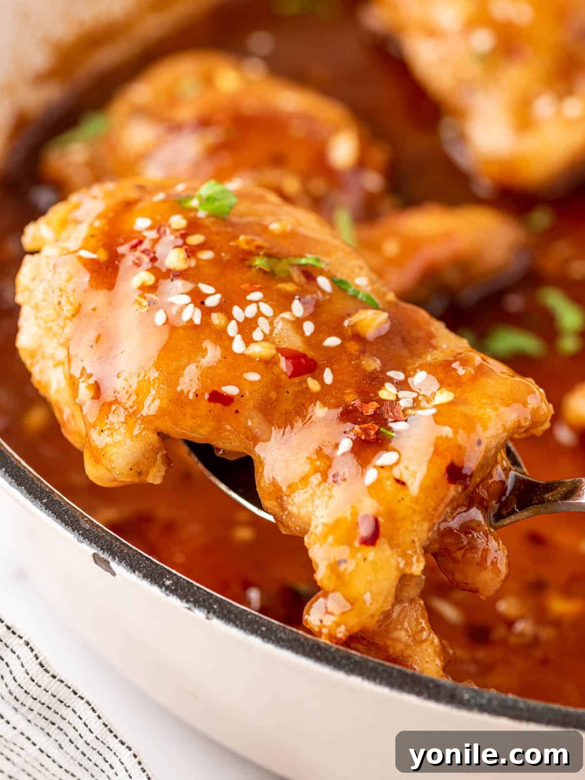 A glistening honey garlic chicken thigh being lifted from the pan with a serving spoon, showcasing its sticky glaze.