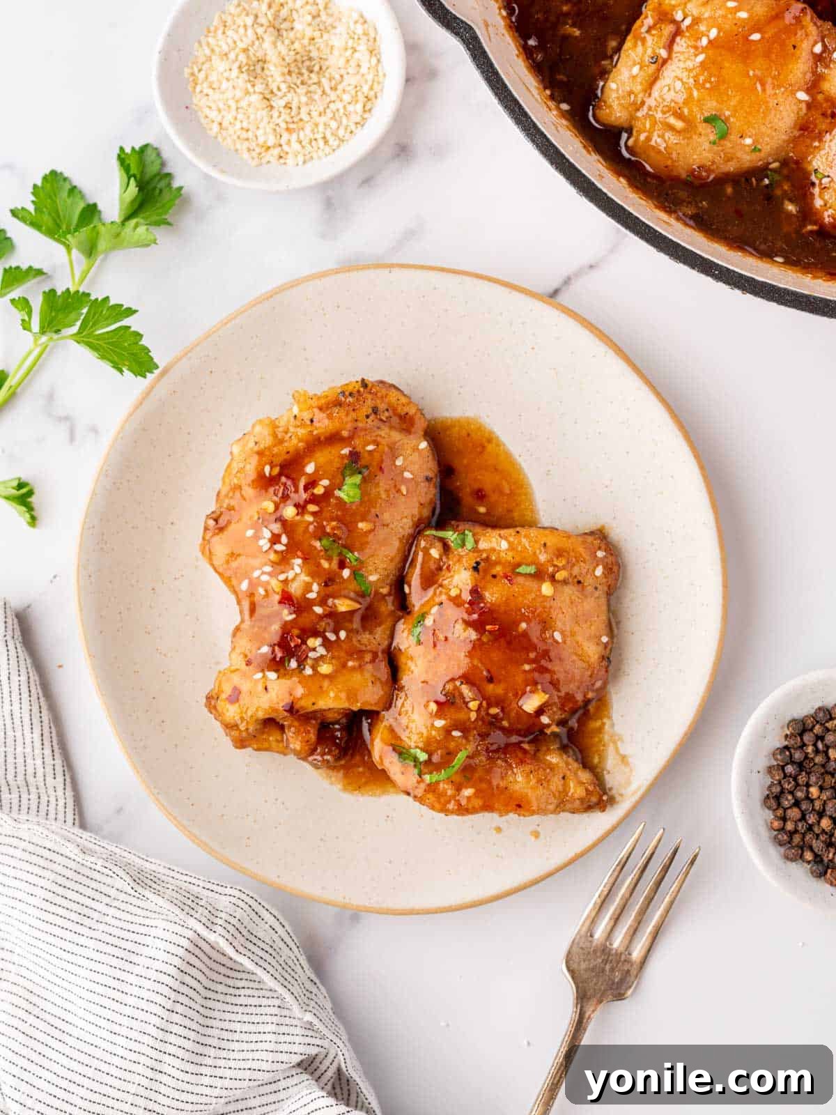 A beautifully plated dish with two honey garlic chicken thighs, garnished with parsley and sesame seeds.