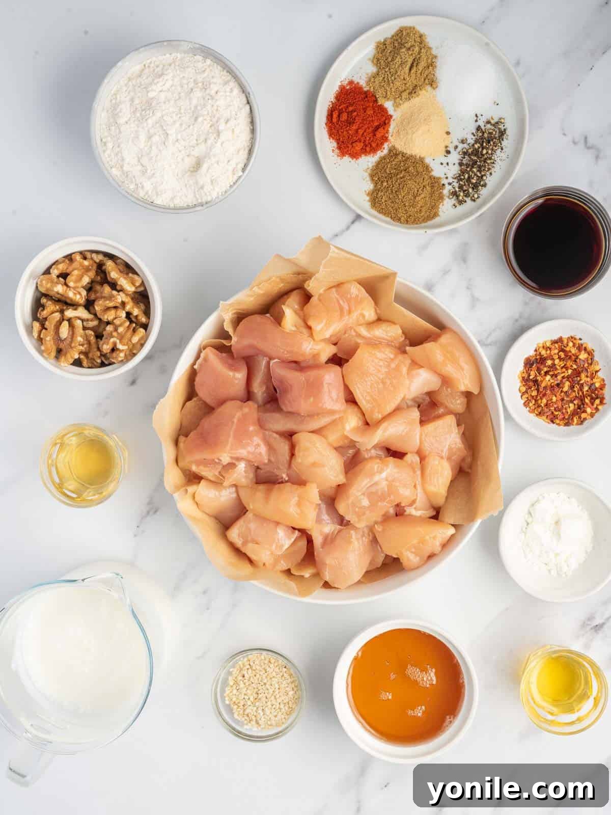 A collection of fresh ingredients laid out, including chicken, walnuts, honey, soy sauce, and spices, for making Honey Walnut Chicken.