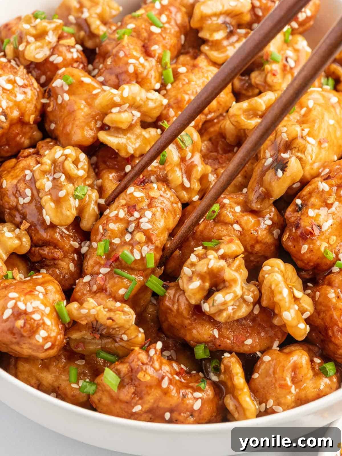 Chopsticks lifting a piece of Honey Walnut Chicken, showcasing its crispy coating and rich sauce.