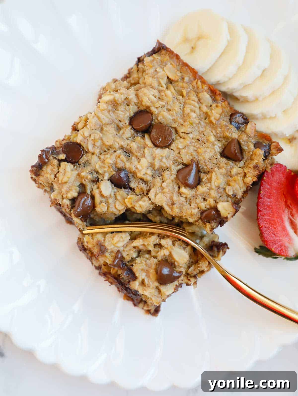 Chocolate Chip Oat Delight 8 A beautifully presented plate with a square of chocolate chip baked oatmeal, fresh raspberries, blueberries, a fork, and a slight drizzle of maple syrup, inviting a delicious breakfast.