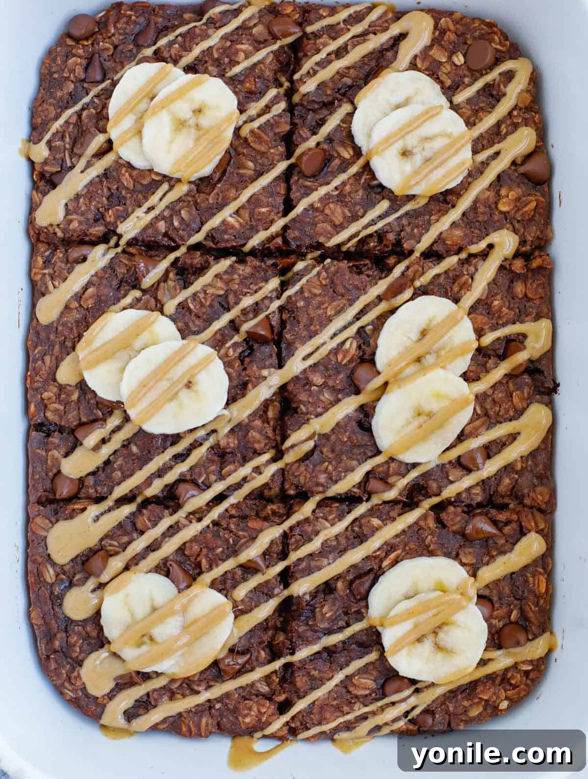 A close-up shot of baked chocolate oats, beautifully topped with fresh slices of banana and a generous drizzle of creamy peanut butter, showcasing its appealing texture and rich color.