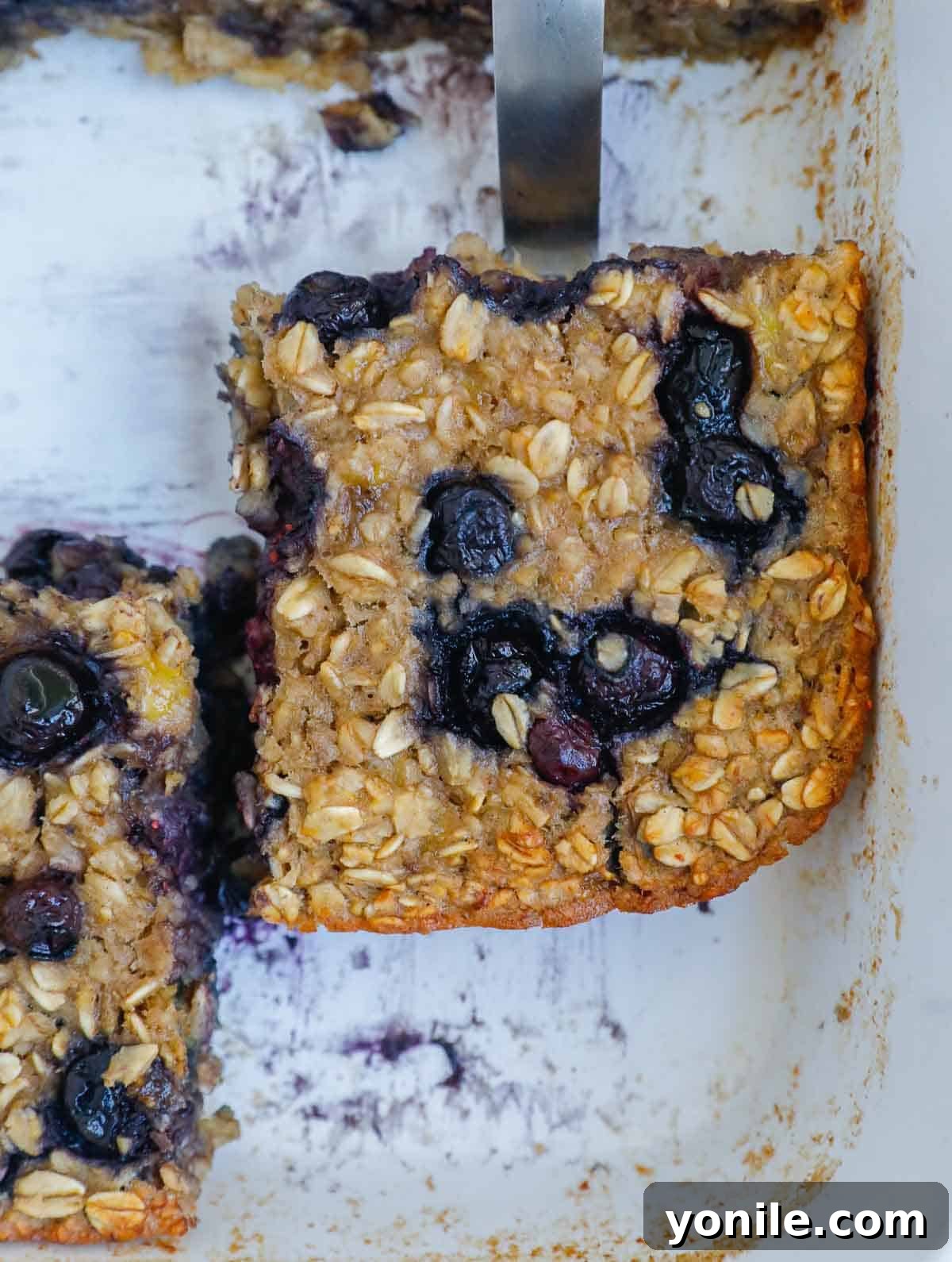 A large portion of baked oatmeal in a baking dish, showcasing its hearty texture and generous blueberry distribution.