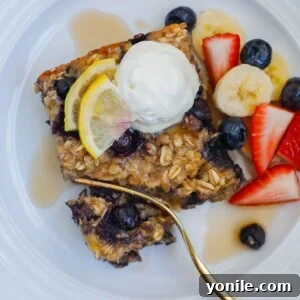 A square of blueberry oatmeal bake on a plate topped with whipped cream and fresh fruit.