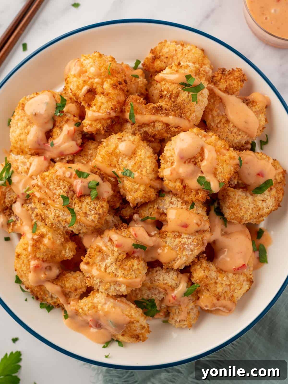 A vibrant pile of golden, crispy air fryer panko shrimp generously drizzled with creamy Bang Bang sauce and garnished with fresh parsley, ready to be served.