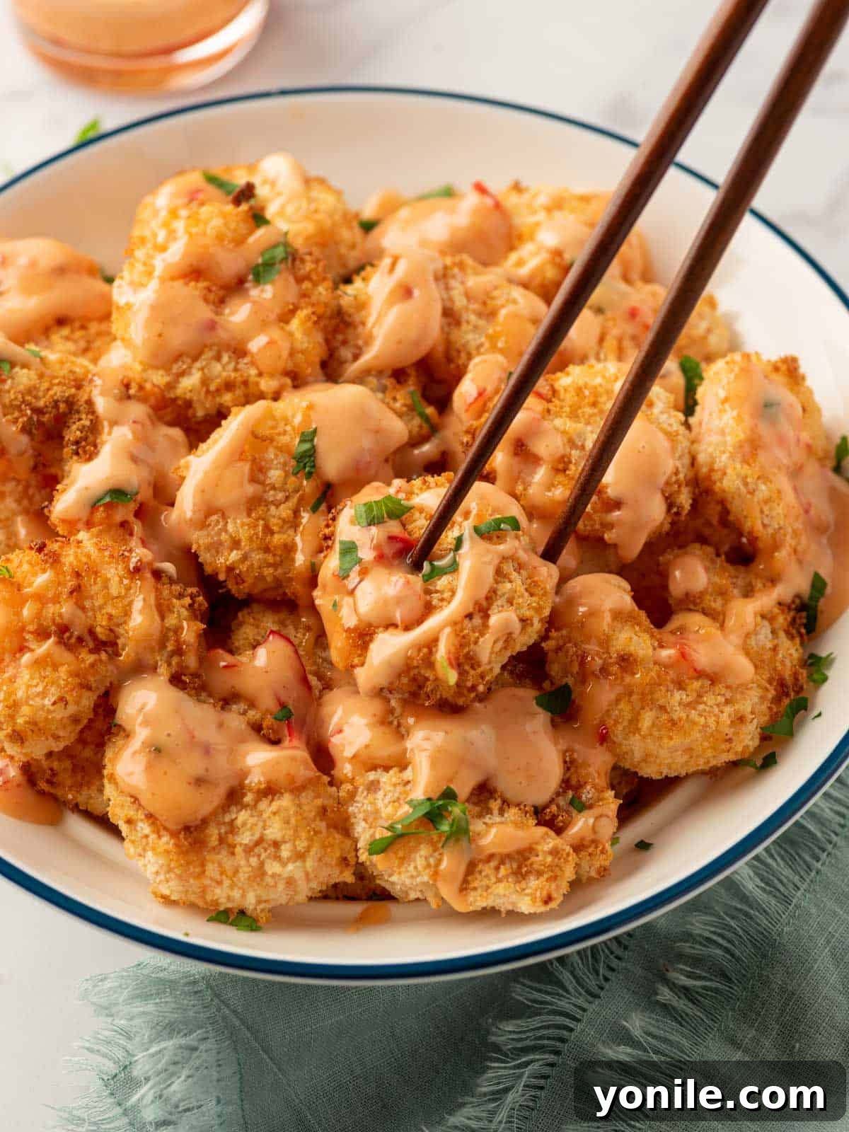 A beautifully arranged plate of crispy air-fried Bang Bang shrimp, garnished with parsley, accompanied by chopsticks and a small dish of extra sauce.