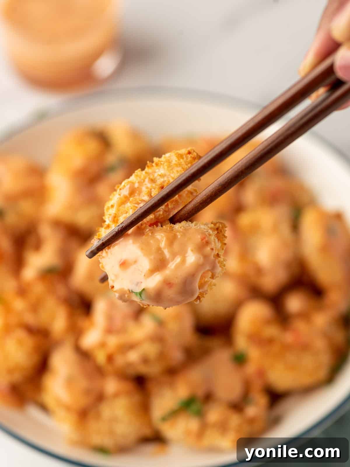A pair of chopsticks holding up a single piece of perfectly crunchy air fryer Bang Bang shrimp, showcasing its golden coating and inviting texture.