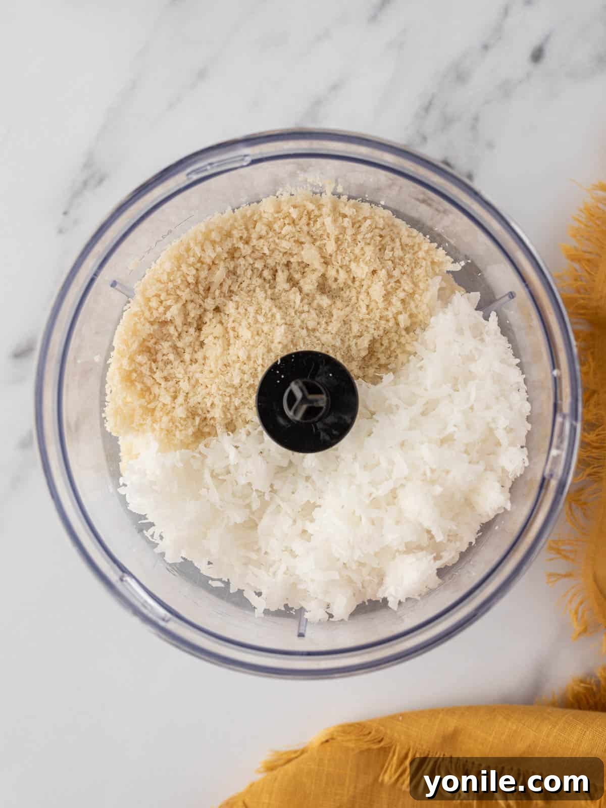 A close-up view of a bowl containing the prepared mixture of pulsed coconut flakes and panko breadcrumbs, ready for coating the shrimp.