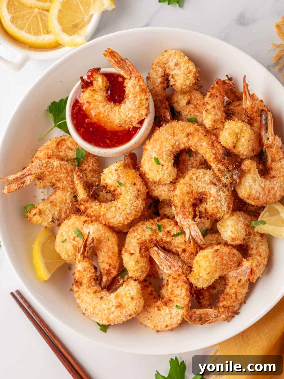 A close-up of a plate piled high with perfectly golden and crispy air fryer shrimp, ready to be served.