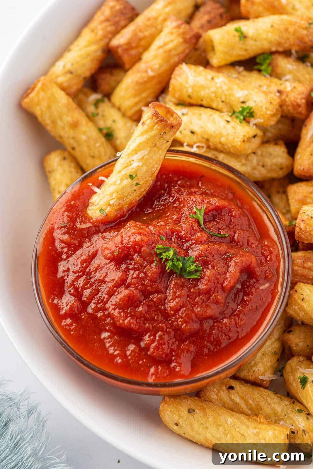 A plate of fried pasta chips with one fried noodle dipping into marinara sauce.