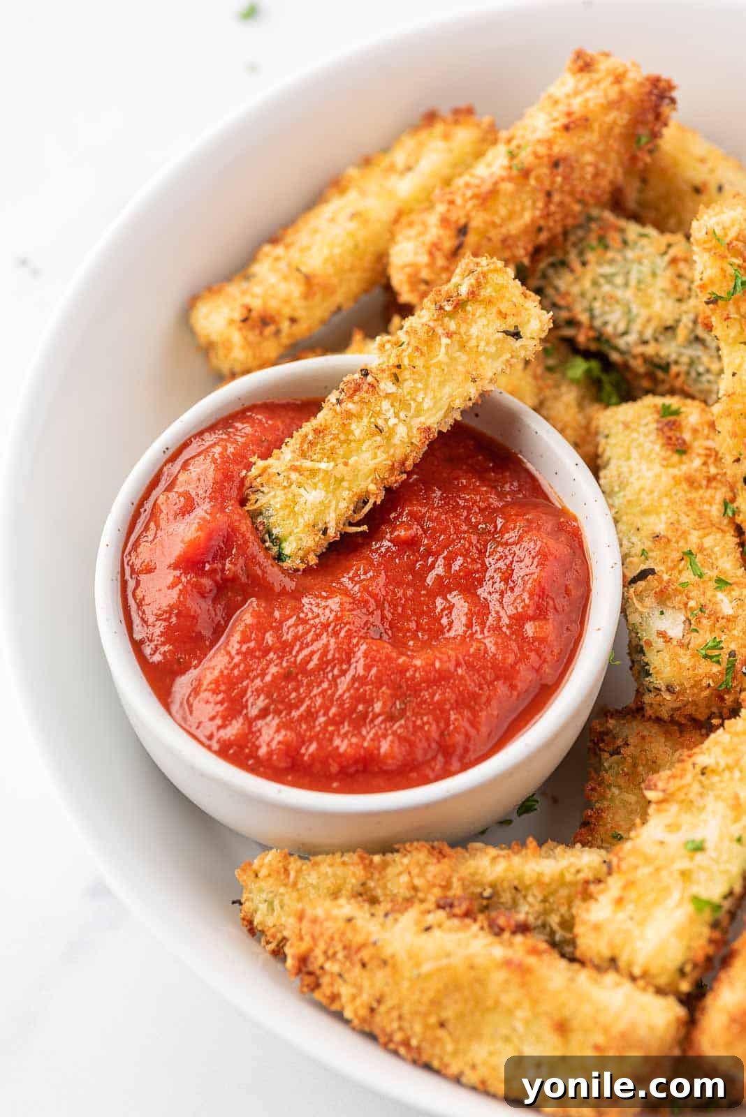 Crispy Air Fryer Zucchini Sticks 7 A plate of crispy zucchini fries with one zucchini dunked in marinara.
