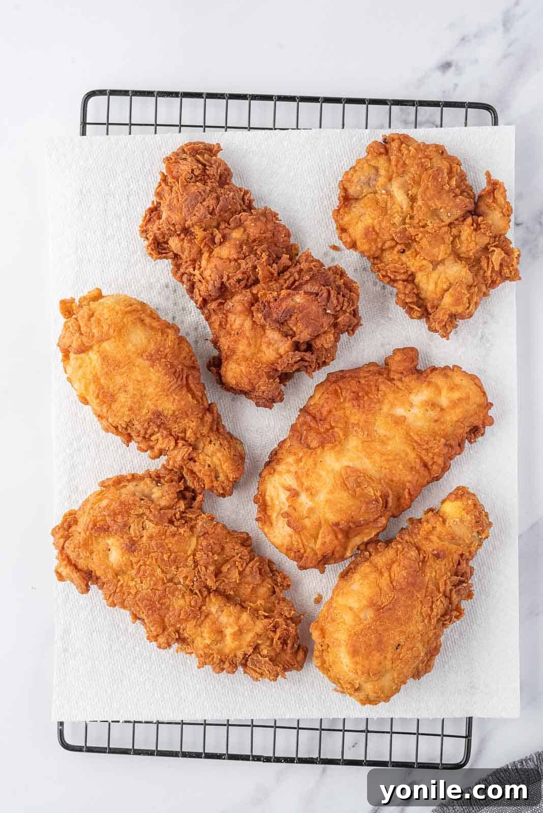 Extra crispy fried chicken draining on paper towels on a wire rack.