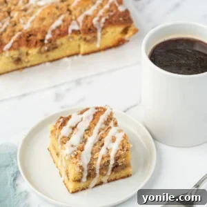 A slice of keto coffee cake on a white plate next to a cup of coffee and a fork. A tray of almond flour coffee cake sits in the background.