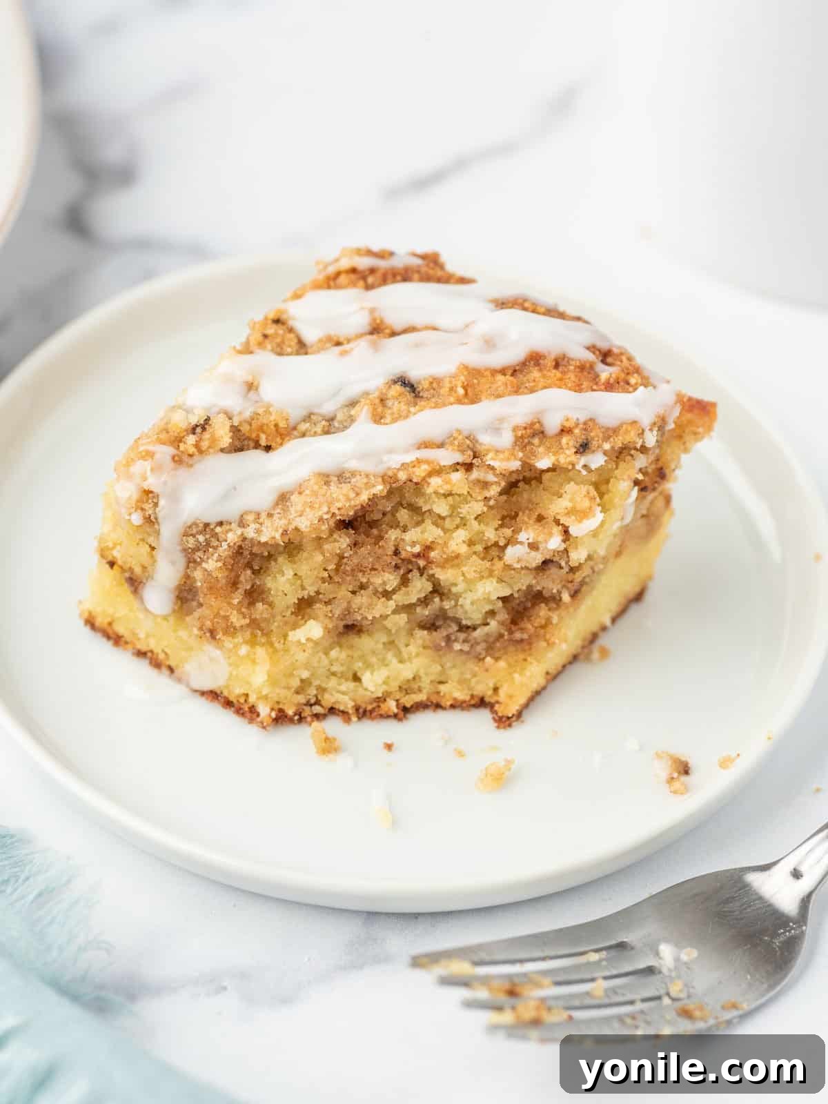 A tantalizing piece of low carb coffee cake, with a small bite missing, sits enticingly on a white plate, accompanied by a few crumbs and a fork to the side, highlighting its delicious texture.