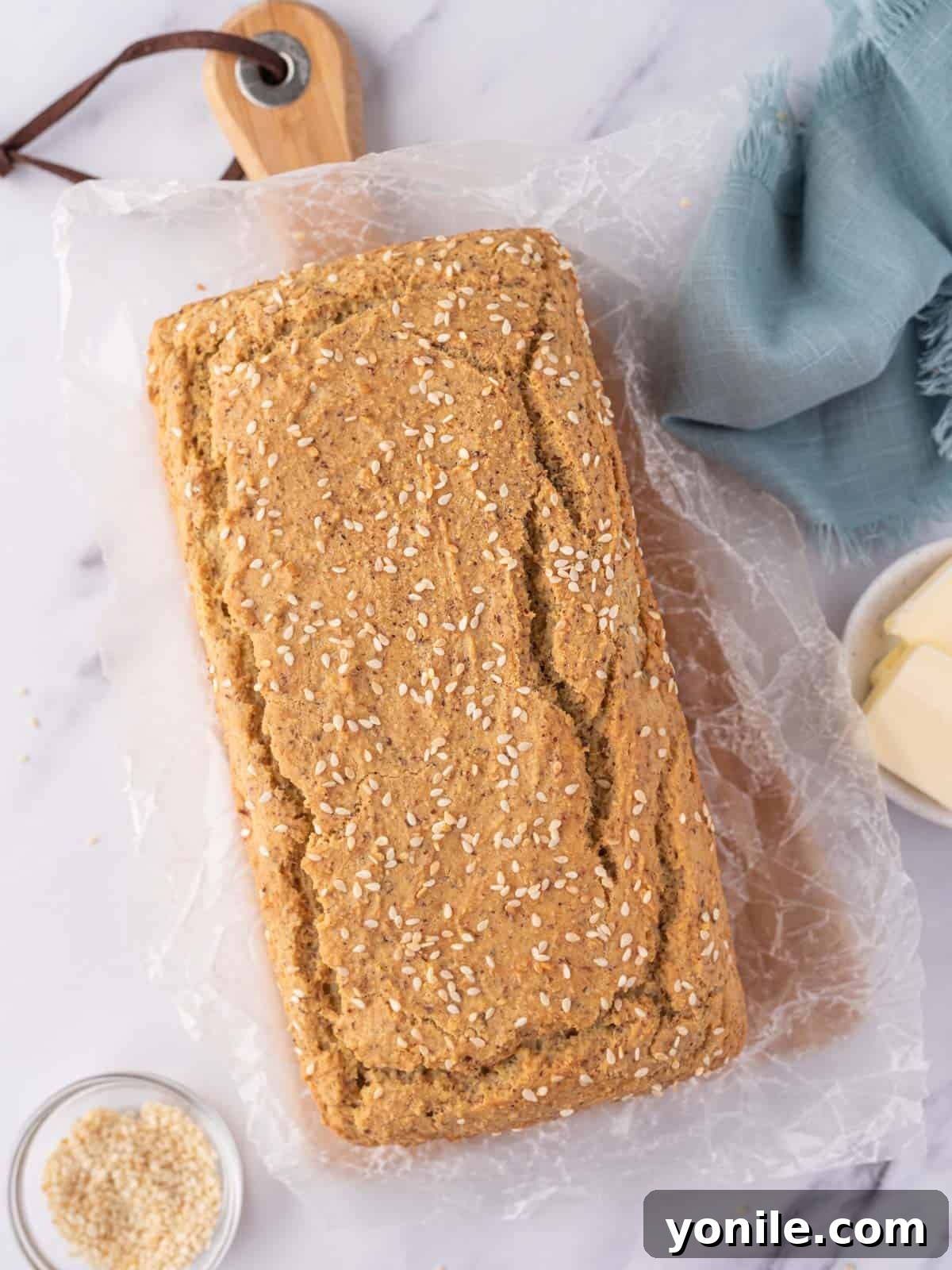 Guilt-Free Keto Sandwich Loaf 2 A loaf of low carb sandwich bread topped with sesame seeds rests on a wax paper covered bread board.
