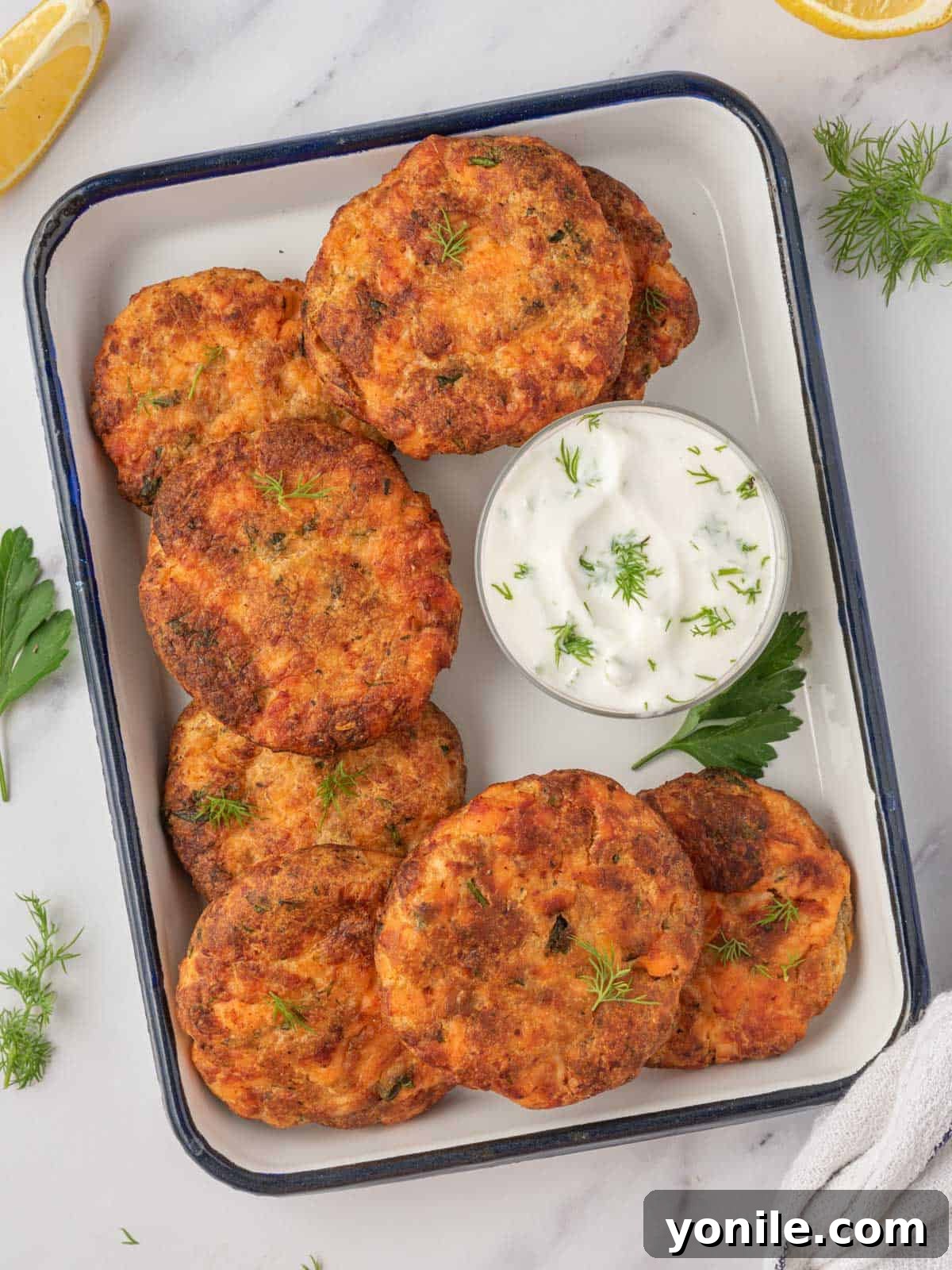 A tray of golden, crispy air fryer salmon patties with a small bowl of creamy tzatziki sauce on the side, ready to be served.