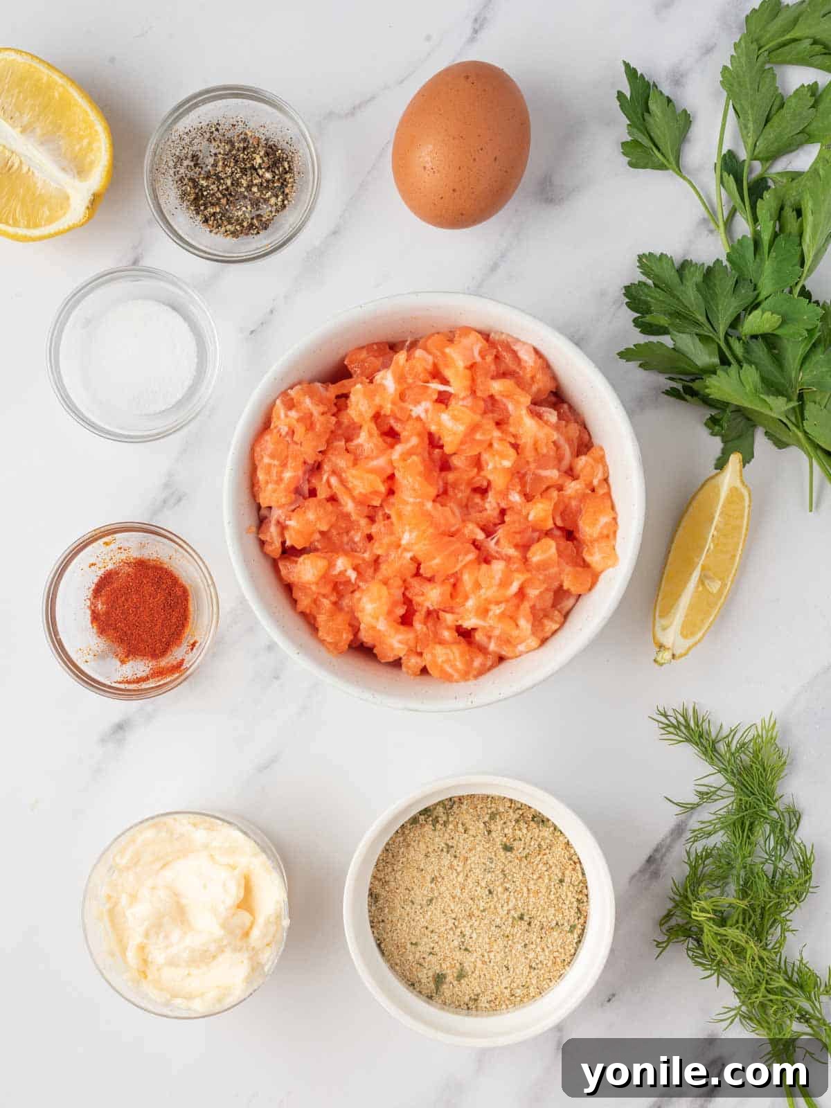 Fresh ingredients laid out for making salmon patties, including salmon fillets, eggs, bread crumbs, mayonnaise, lemon, and fresh herbs.