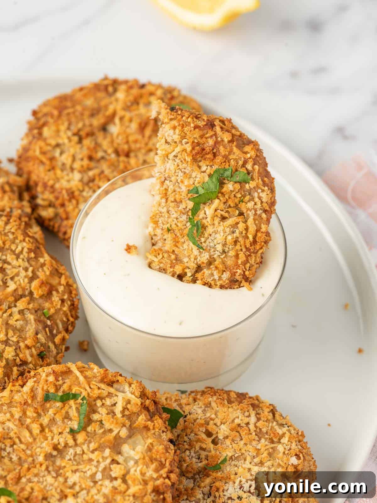 A piece of air fryer tuna patties is dunked into dip.