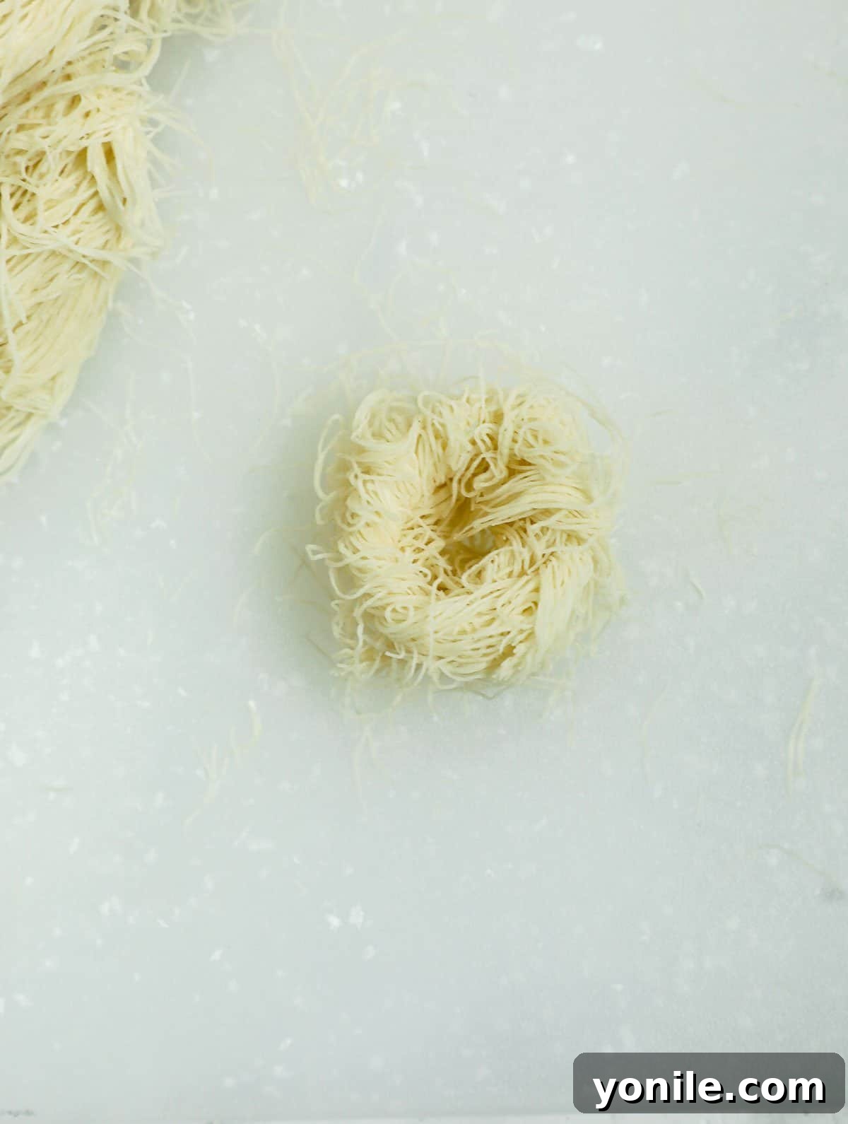 Close-up of baklava phyllo dough being shaped into a bird nest before adding pistachios.