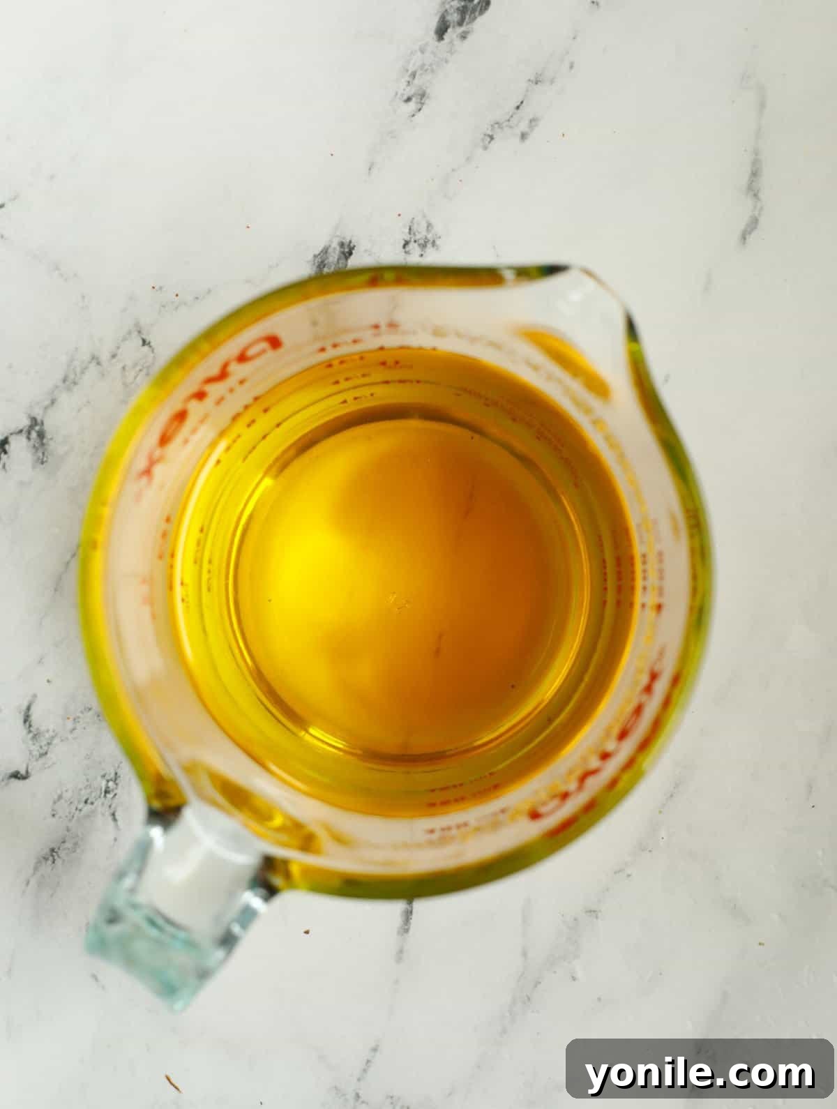 Melted ghee in a clear glass measuring cup, ready to be poured over the baklava nests.