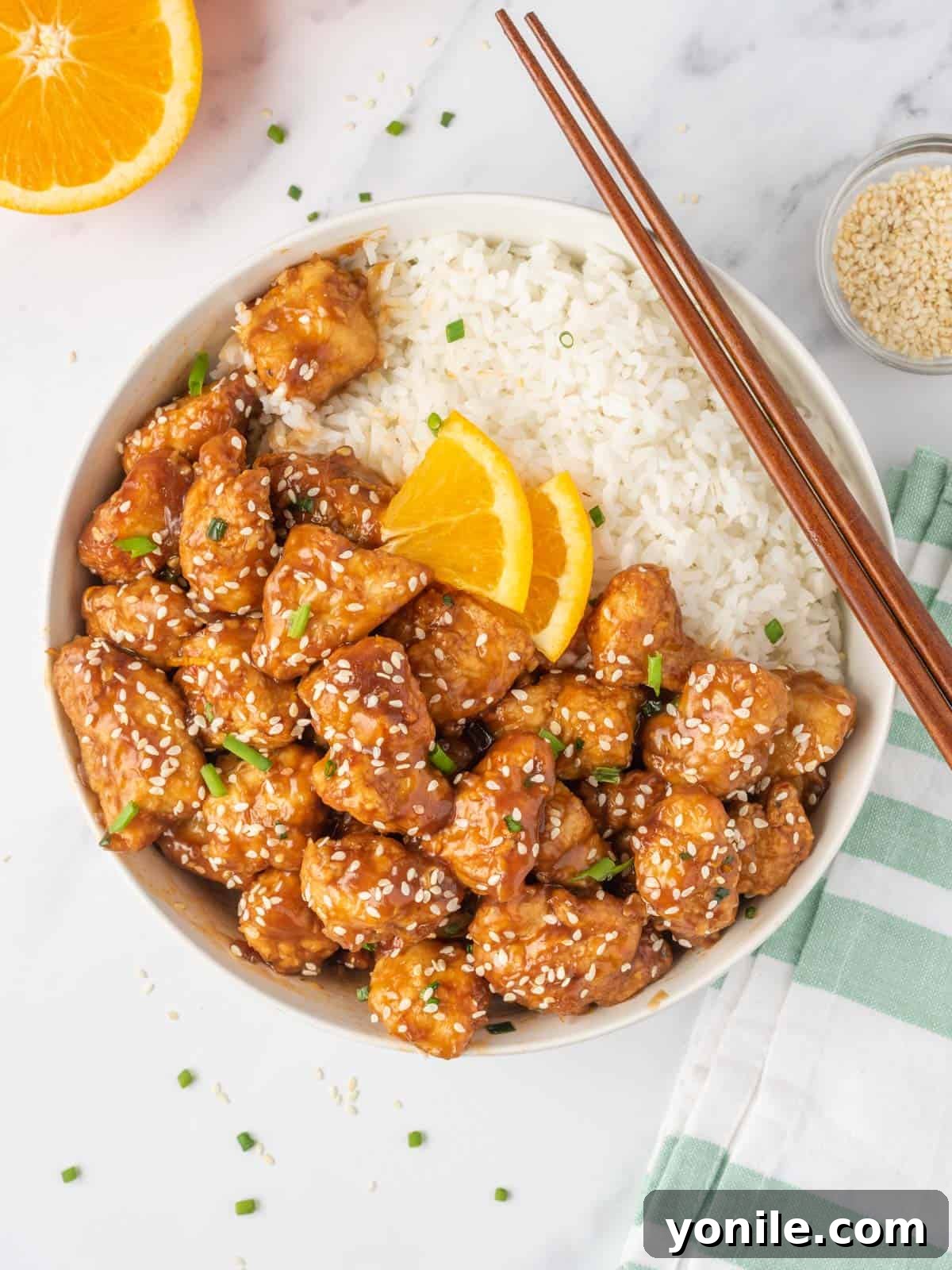 A bowl of crispy air fryer orange chicken served with rice and chopsticks.