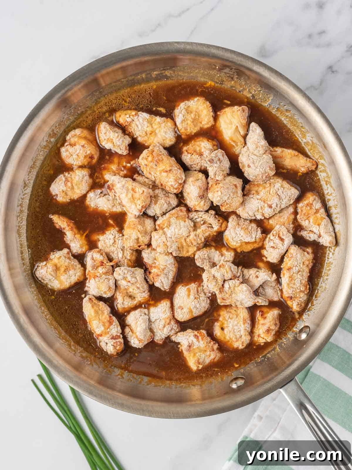 Tossing crispy air fried chicken with the easy orange chicken sauce in a skillet.