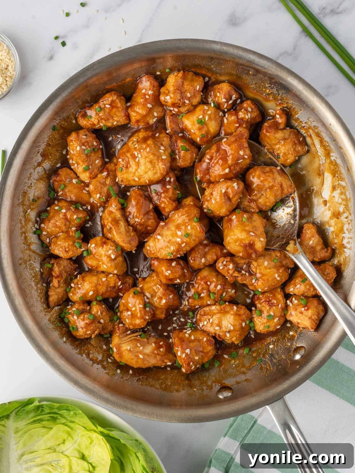 Air fryer orange chicken in a skillet with a serving spoon, showcasing the delicious glaze.