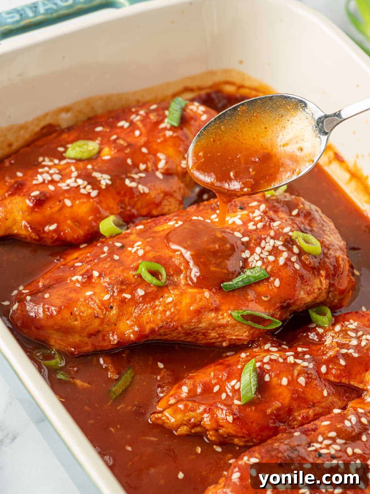 Spooning honey sriracha sauce over baked chicken breast after cooking, enhancing its glaze.
