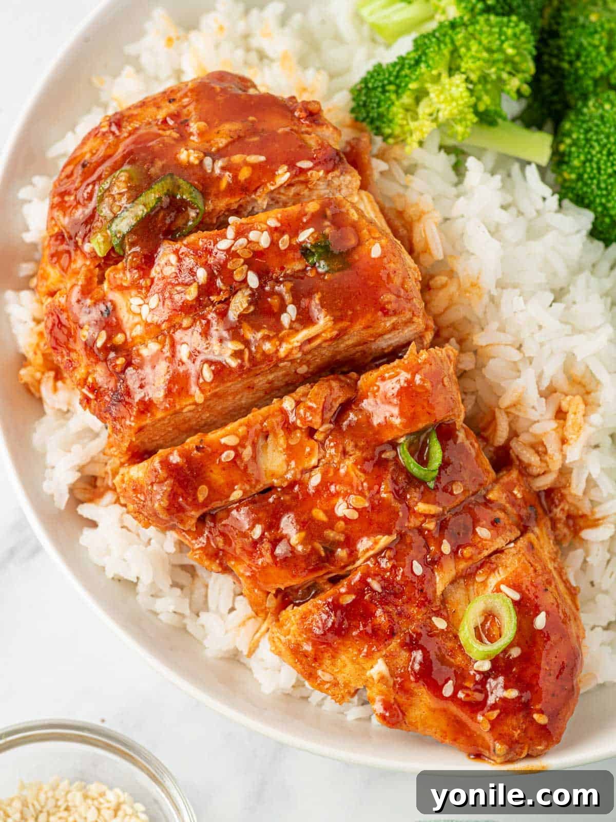 Sliced honey sriracha baked chicken breast served over rice with a side of greens.