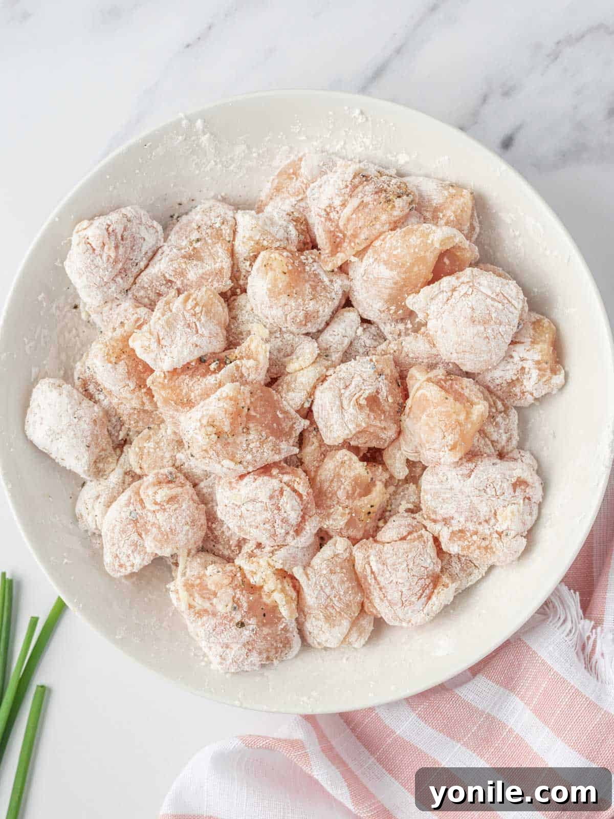Cubed chicken breast meticulously dredged in cornstarch, ensuring a crispy coating for the stir fry.