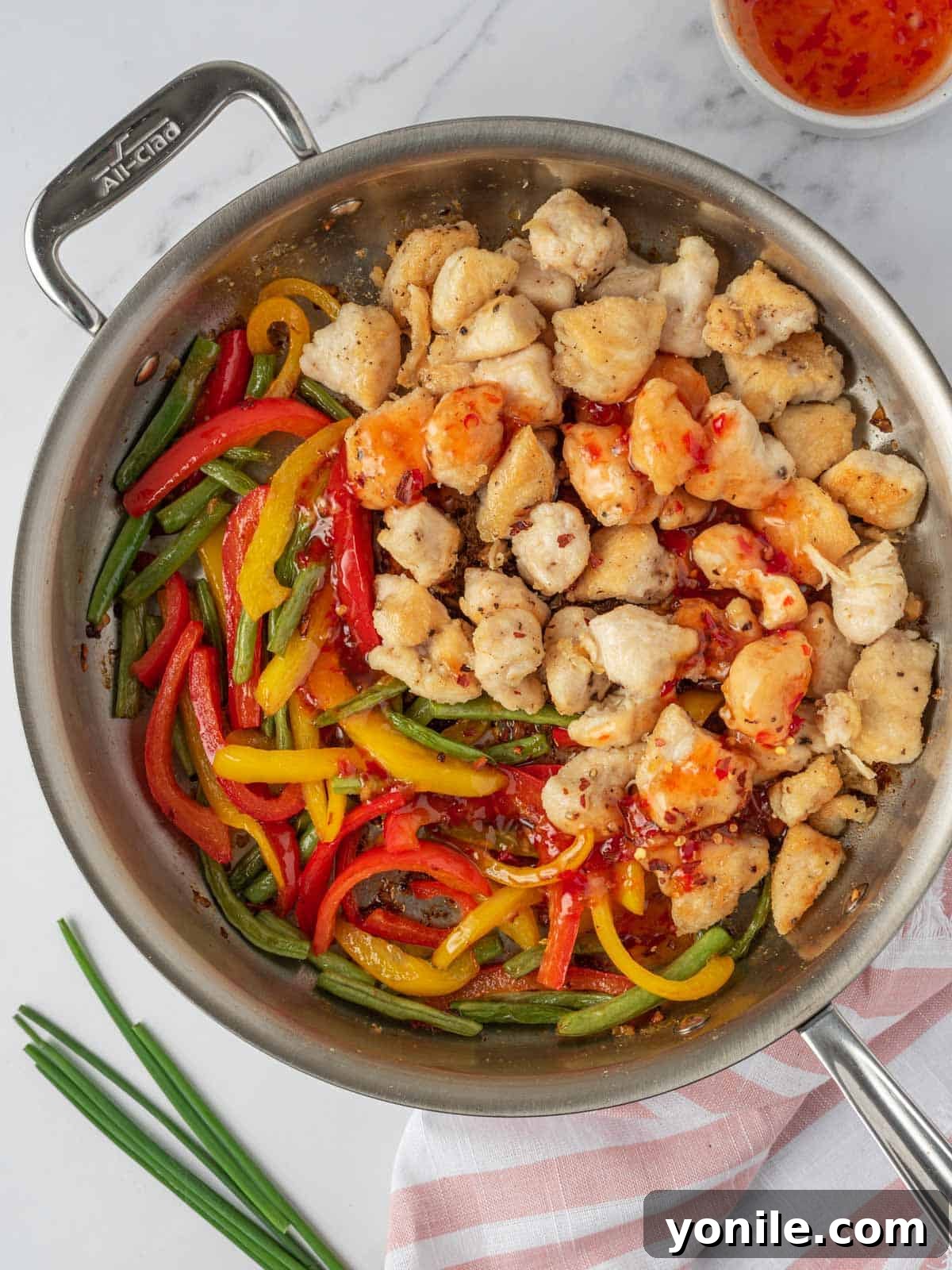Cooked crispy chicken and sautéed vegetables combined in a skillet, about to be coated in sweet Thai chili sauce.